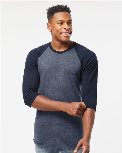 Load image into Gallery viewer, A young man smiles, wearing a Tultex Fine Jersey Raglan T-Shirt with a dark blue body and black sleeves, crafted from ring-spun cotton. His left arm is slightly bent against a plain white background.