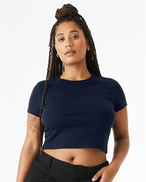 Load image into Gallery viewer, A person with long braided hair stands confidently in a BELLA + CANVAS Women's Micro Rib Baby Tee, paired with black pinstripe pants. They have a floral tattoo on their left arm against a plain white background.