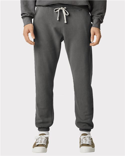 Load image into Gallery viewer, A person wears Comfort Colors - Garment-Dyed Lightweight Fleece Sweatpants in dark gray, featuring a drawstring waistband, crafted from ring-spun cotton, paired with a black sweater and white/olive green sneakers against a plain light gray background.