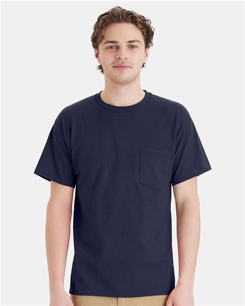 Load image into Gallery viewer, A person with short, wavy brown hair is wearing a plain navy blue Hanes Essential-T Pocket T-Shirt, crafted through socially conscious manufacturing. They are standing against a light gray background.