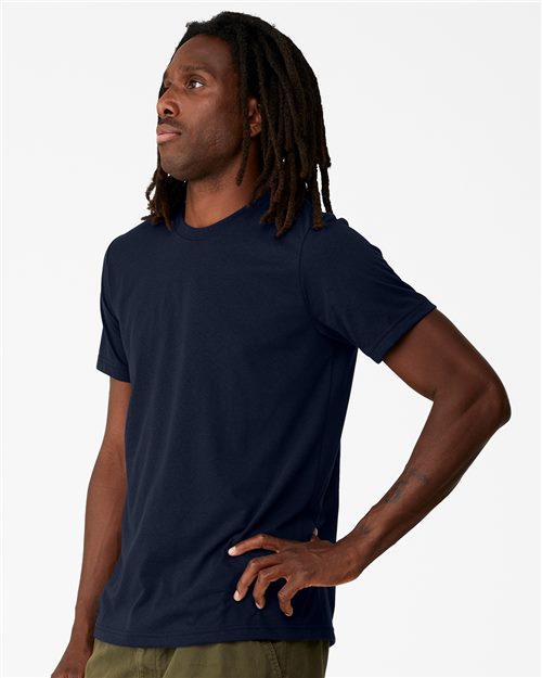Load image into Gallery viewer, A person with long hair confidently stands in a sustainable BELLA + CANVAS EcoMax Tee and olive green pants made from recycled polyester, one hand on their hip, looking upwards to the left against a plain white backdrop.
