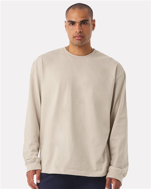 Load image into Gallery viewer, Wearing the BELLA + CANVAS 7.5 oz Heavyweight Long Sleeve Tee in beige and dark pants crafted with Blue Sign certified dyes, a person stands against a plain white background. With a neutral expression, they embody a unisex silhouette that exudes timeless sustainability while looking straight ahead.