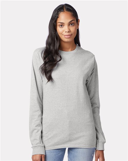 Load image into Gallery viewer, A person with long dark hair, wearing the Hanes Authentic Long Sleeve T-Shirt made of plain gray 100% cotton and blue jeans, stands against a light gray background. They face the camera with a neutral expression, highlighting sustainable manufacturing.