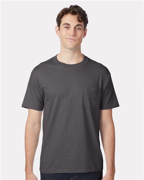 Load image into Gallery viewer, A person in a dark gray Hanes Beefy-T® Pocket T-Shirt, made from ring-spun cotton, stands against a white background, smiling with short, wavy hair and wearing dark pants.