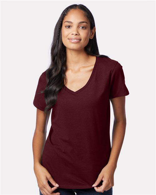 Load image into Gallery viewer, A long-haired person wearing a maroon Hanes Perfect-T Women’s V-Neck T-Shirt made from ring-spun cotton and jeans stands against a plain light gray background, appearing relaxed with their arms at their sides.