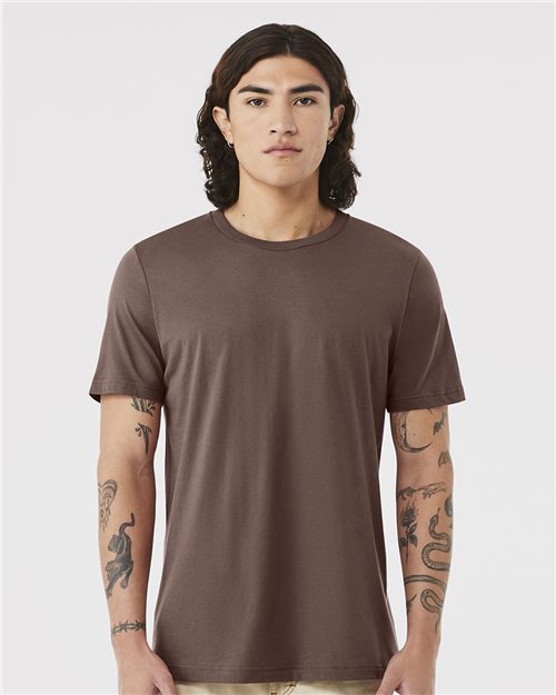 Load image into Gallery viewer, A person with long, dark hair faces forward wearing a plain brown BELLA + CANVAS - Jersey Tee made from Airlume combed cotton. Arm tattoos are visible as they stand neutrally against a light gray background. The unisex sizing of the shirt ensures it's versatile for all.