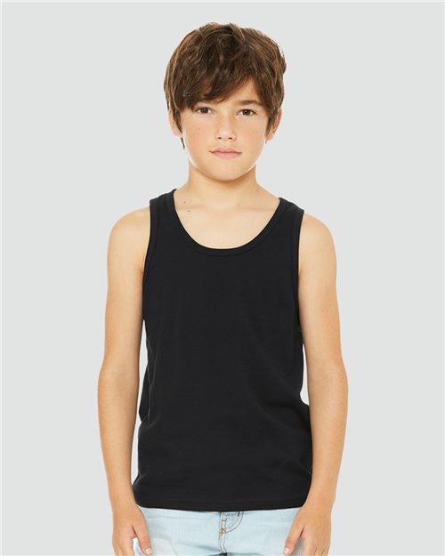 Load image into Gallery viewer, A child stands against a grey background, wearing the BELLA + CANVAS - Youth Jersey Tank made from Airlume combed cotton and light blue jeans. With short brown hair and a calm expression, they showcase unisex sizing and the sustainable fashion promise of BELLA + CANVAS.