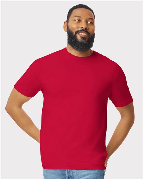 Load image into Gallery viewer, A man wearing a Gildan Softstyle® T-Shirt in red, made from ring-spun cotton, along with blue jeans stands with hands in pockets against a plain light gray background.