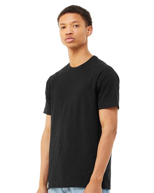 Load image into Gallery viewer, A person in a solid black BELLA + CANVAS Heather CVC Raglan Tee and light blue jeans stands against a white backdrop, facing slightly left. Sporting short hair and a neutral expression, they exemplify sustainable manufacturing with an ideal retail fit.