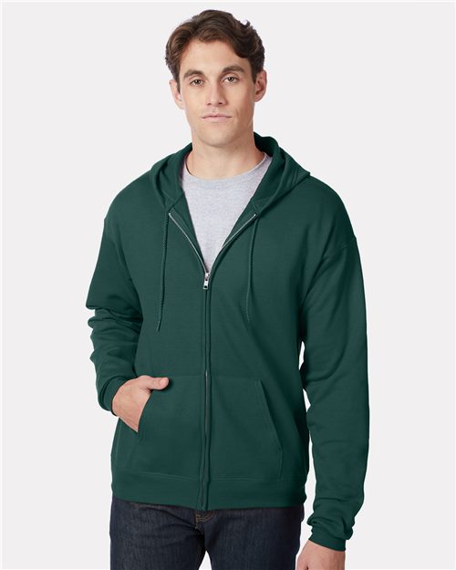 Load image into Gallery viewer, A person in a dark green Hanes - Ecosmart® Full-Zip Hooded Sweatshirt, a light gray T-shirt, and dark jeans stands against a plain background with one hand in their pocket and a neutral expression.