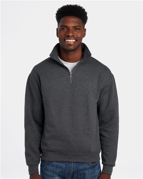 Load image into Gallery viewer, A smiling person wearing a JERZEES - Super Sweats NuBlend® Quarter-Zip Cadet Collar Sweatshirt in dark gray stands against a white background. The sweater features socially conscious manufacturing, pill-resistant fleece, and a high collar while they rest their hands by their sides over a white shirt and blue jeans.