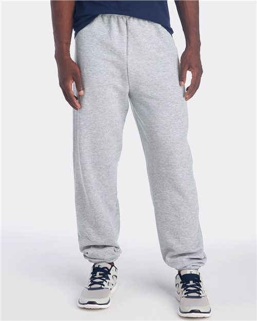 Load image into Gallery viewer, A person in a navy shirt, gray JERZEES - NuBlend® Sweatpants, and running shoes stands against a plain white background, showing only the lower half of the body.