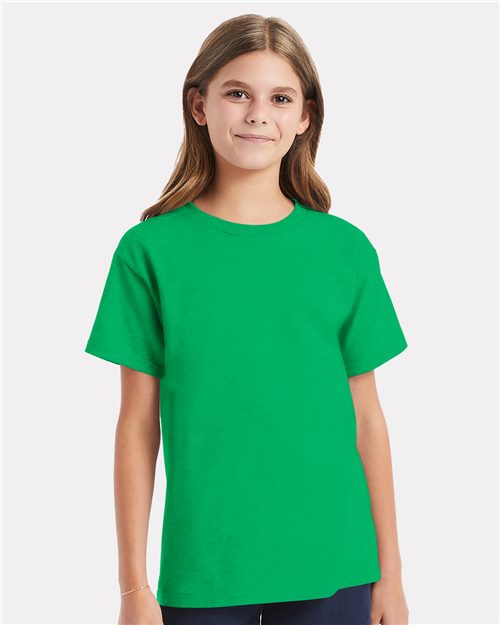 Load image into Gallery viewer, A girl wearing a vibrant green "Hanes - Essential-T Youth T-Shirt" and dark pants smiles against a plain light gray background.