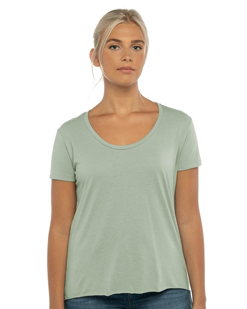 A person with long blonde hair is wearing a light green Next Level - Women's Festival Scoop Neck T-Shirt and blue jeans, standing against a white background.