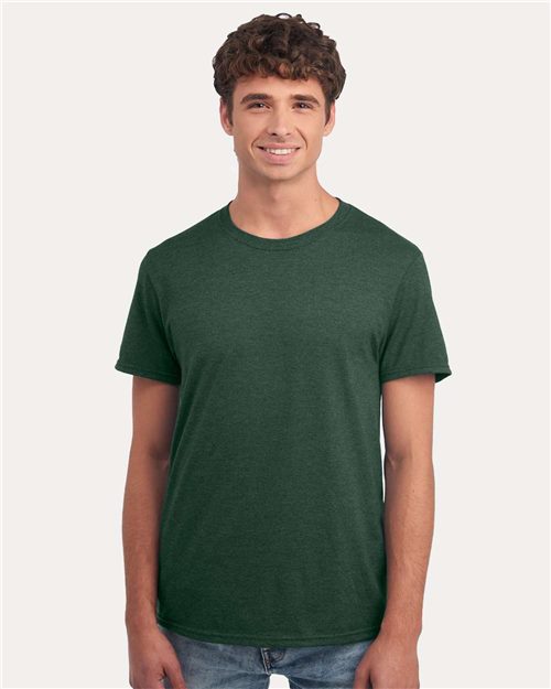Load image into Gallery viewer, A person wearing a dark green JERZEES - Premium Blend Ring-Spun T-Shirt and jeans smiles against a plain light background. They have curly hair and a relaxed posture.