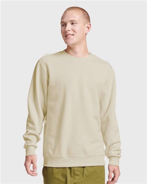 Load image into Gallery viewer, A person in a JERZEES Eco™ Premium Blend Ring-Spun Crewneck Sweatshirt and olive green pants stands against a plain gray background, smiling and looking slightly to the side.
