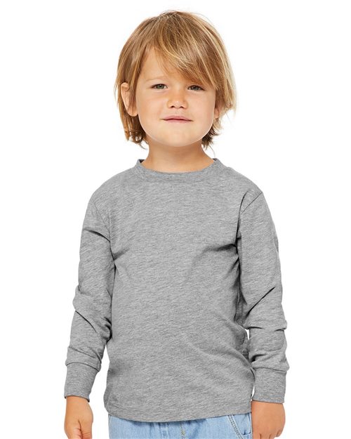 Load image into Gallery viewer, A young child with light brown hair is facing the camera, wearing a BELLA + CANVAS Toddler Jersey Long Sleeve Tee, gray in color and crafted from Airlume cotton, paired with light blue jeans against a plain white background.