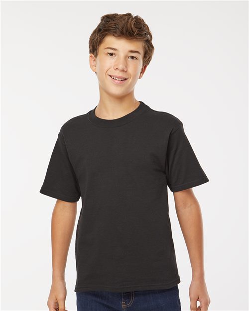 Load image into Gallery viewer, A boy in an M&O Youth Gold Soft Touch T-Shirt, matched with blue jeans, stands against a white background, smiling with his hands slightly away from his sides.