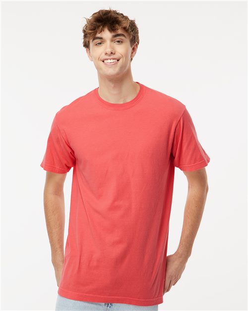 Load image into Gallery viewer, A person with short, curly hair is smiling and wearing a M&O Vintage Garment-Dyed T-Shirt. It’s coral and made of ring-spun cotton. They also have light blue jeans on and are standing against a plain white background.