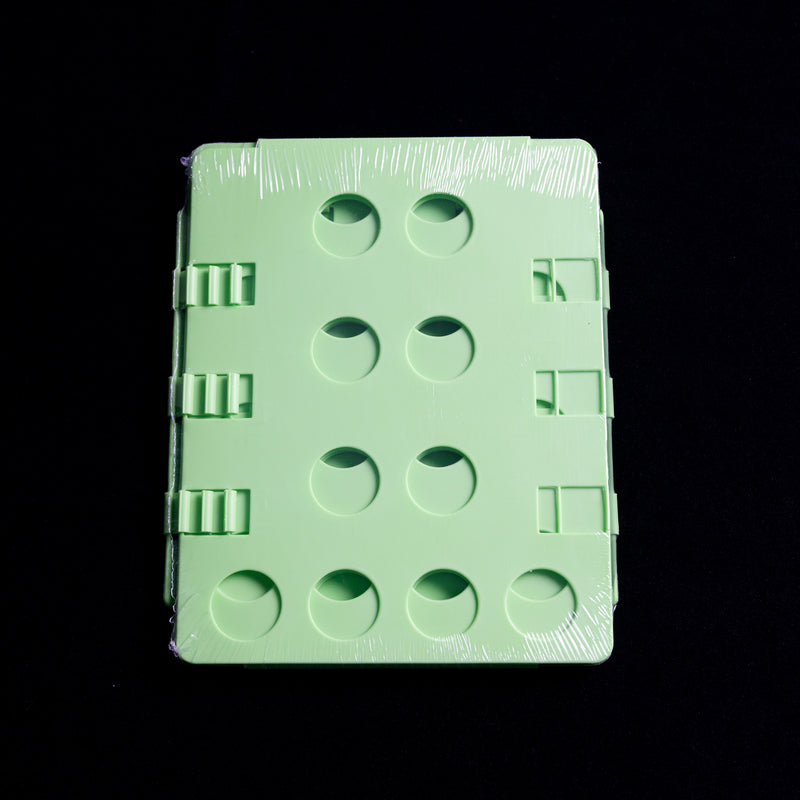 Load image into Gallery viewer, A Shirt Folder by Quick Transfers, featuring circular indents in green plastic, is wrapped in clear packaging and set against a black background.