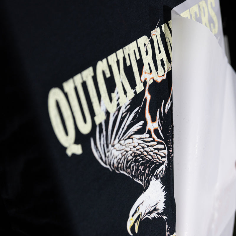 Load image into Gallery viewer, Close-up of a black tee showcasing a bold eagle graphic and "EQUICKARIO,” partially revealed as glossy white paper peels away, highlighting the exceptional detail from Quick Transfers' FASTFILM™ DTF TRANSFERS - Build a Gang Sheet, created with direct to film transfers.