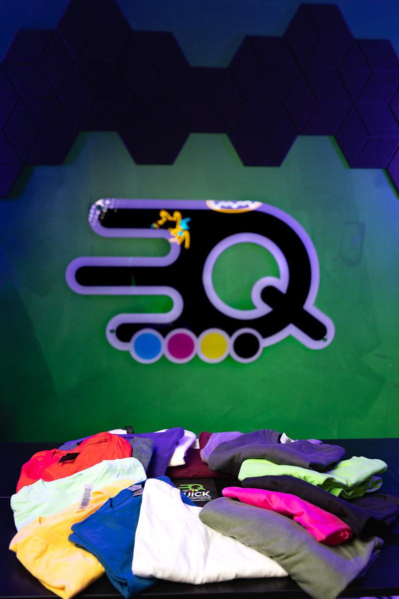 Load image into Gallery viewer, A selection of colorful Short Sleeve Shirt Mystery Bundles from Quick Transfers is displayed on a table before a green wall with the brand’s stylized three-dot ‘Q’ logo, highlighting new samples for the upcoming clearance sale.