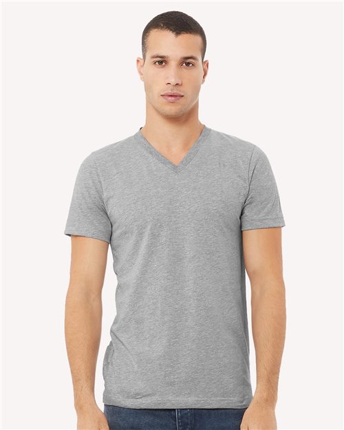 Load image into Gallery viewer, A person with short hair wears a gray BELLA + CANVAS Heather CVC V-Neck Tee and blue jeans, standing against a plain white background. The unisex sizing complements their look as they gaze directly at the camera with a neutral expression.
