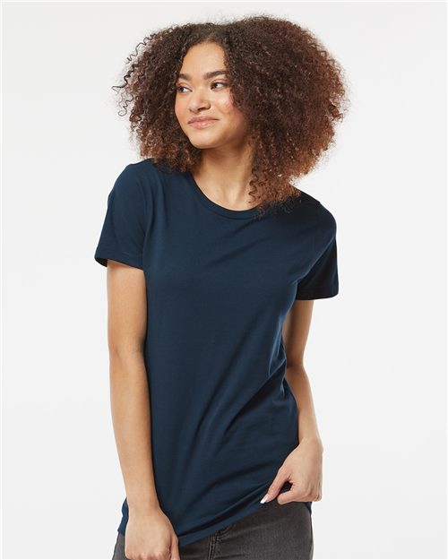 A curly-haired person smiles and looks aside, showcasing a Tultex Women's Premium Cotton T-Shirt in dark blue and gray pants, set against a plain white background.