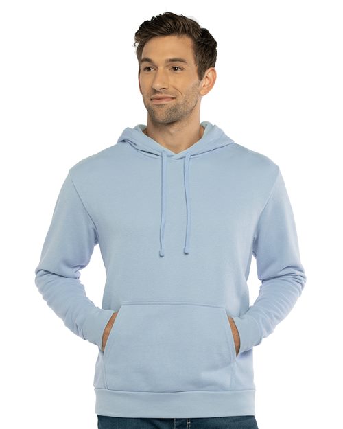 Load image into Gallery viewer, A person dons the light blue &quot;Laguna Sueded Hoodie&quot; by Next Level, crafted from sustainable cotton/polyester fleece. With a drawstring hood, long sleeves, and a front pocket, they exude comfort as they smile slightly against a plain white background.
