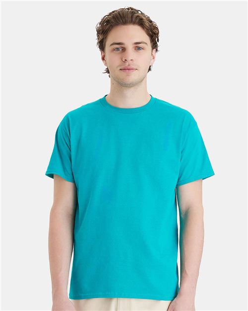 A person wearing a Hanes - Essential-T T-Shirt in bright turquoise, made through sustainable manufacturing, stands against a plain white background and looks directly at the camera with a neutral expression.