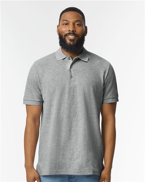 A person in a Gildan - Hammer™ Pique Polo and blue jeans stands confidently against a plain white background.