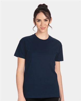 A person with dark hair tied up is wearing the Next Level - Women's Cotton Relaxed T-Shirt by Next Level, in plain navy blue, made from 100% combed ring-spun cotton. They stand against a light grey background, smiling slightly at the camera with their hands by their sides.