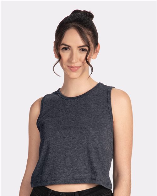 A woman in a Next Level Women's Festival Crop Tank, a relaxed-fit sleeveless charcoal gray top, smiles against a plain white background. Her updo hairstyle with loose strands complements the feminine drape of her attire.