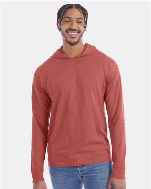 Load image into Gallery viewer, Wearing a ComfortWash by Hanes Garment-Dyed Jersey Hooded Long Sleeve T-Shirt in coral and blue jeans, someone stands smiling against a plain light gray background.
