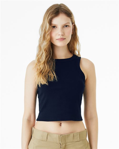 A person with long wavy hair wears a BELLA + CANVAS Women's Micro Rib Racer Tank in black and beige pants, standing against a white background, looking directly at the camera.