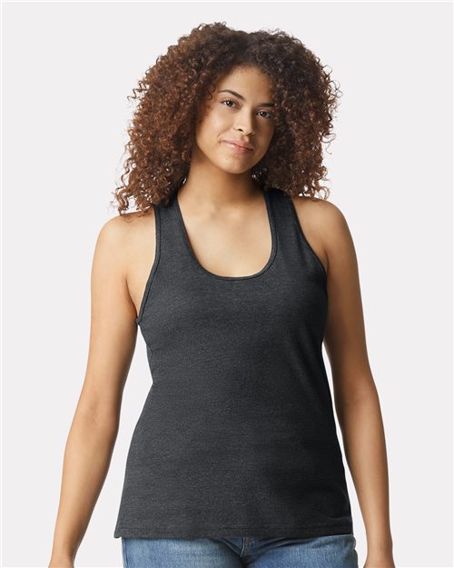 Load image into Gallery viewer, A person with curly hair wears a Gildan Softstyle® Women’s CVC Racerback Tank Top and blue jeans, standing before a plain gray background. Their relaxed expression conveys a commitment to sustainable manufacturing, as they gaze slightly aside.
