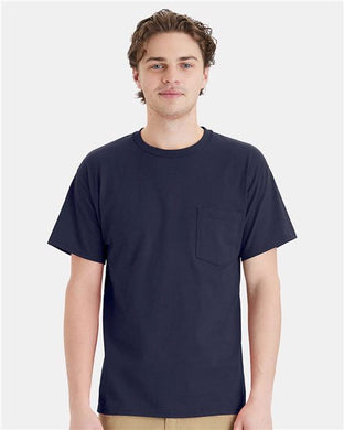 A person with short, wavy brown hair is wearing a plain navy blue Hanes Essential-T Pocket T-Shirt, crafted through socially conscious manufacturing. They are standing against a light gray background.