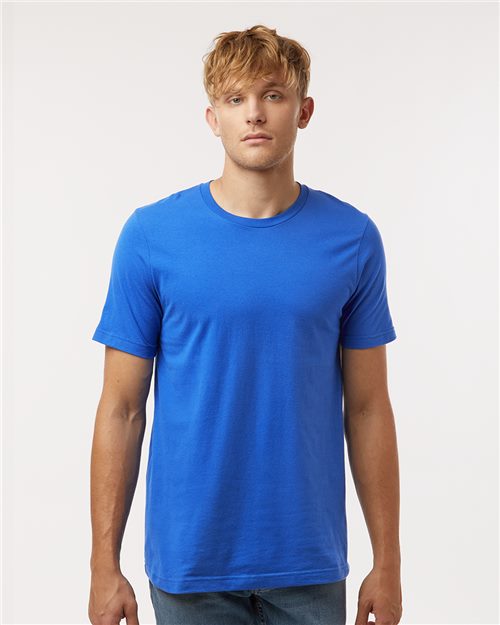 A person with short blond hair is wearing a bright blue Tultex Combed Cotton T-Shirt and jeans, standing against a plain white background.