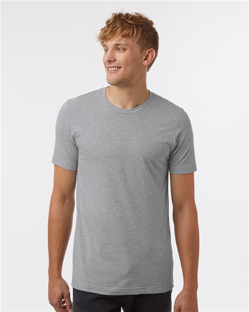 Load image into Gallery viewer, A person with short, blonde hair wearing a Tultex Combed CVC T-Shirt in plain gray stands smiling against a white background.
