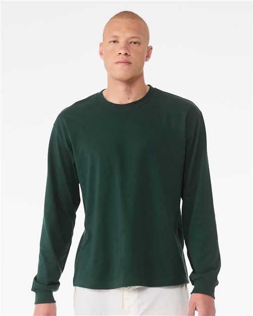 Load image into Gallery viewer, A person with short hair, wearing a BELLA + CANVAS 6 oz. Heavyweight Long Sleeve Tee in dark green and light-colored pants, stands against a plain white background with a neutral expression, hands at their sides, showcasing sustainable manufacturing.
