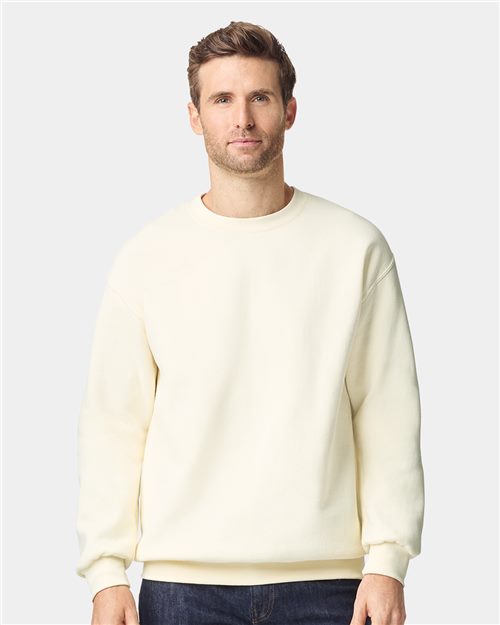 A man with short brown hair wears a Gildan Hammer™ Maxweight Crewneck Sweatshirt, made from recycled polyester, paired with dark jeans. He stands against a light gray background, facing the camera with a neutral expression.