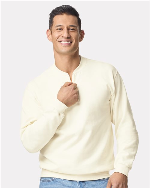 A smiling person with short dark hair is wearing a Gildan Softstyle® Midweight 1/4 Zip Sweatshirt and blue jeans. They stand against a plain white background, gently touching the soft fabric near the collar.