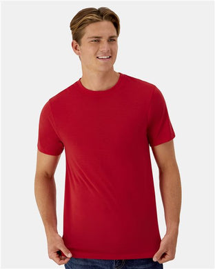 A person with short brown hair smiles in a Hanes - Cool DRI® Cotton Touch T-Shirt, crafted from ring-spun polyester jersey for moisture management. They stand against a light gray background, hands casually by their sides.