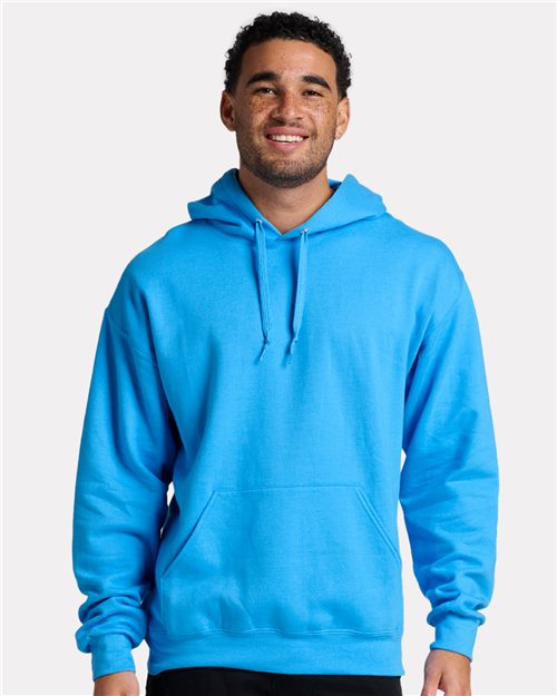 Load image into Gallery viewer, A person smiles against a white background wearing a bright blue JERZEES - Ultimate CVC Hooded Sweatshirt, crafted from sustainably-sourced cotton. The hoodie includes moisture management, a front pocket, and drawstrings.
