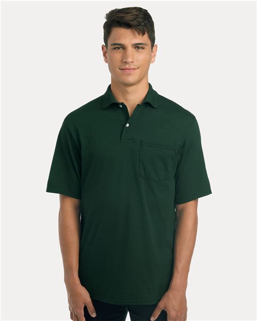 Load image into Gallery viewer, A person is wearing the JERZEES - Dri-Power® dark green polo with a pocket, crafted from sustainably-sourced cotton, against a plain light gray background.
