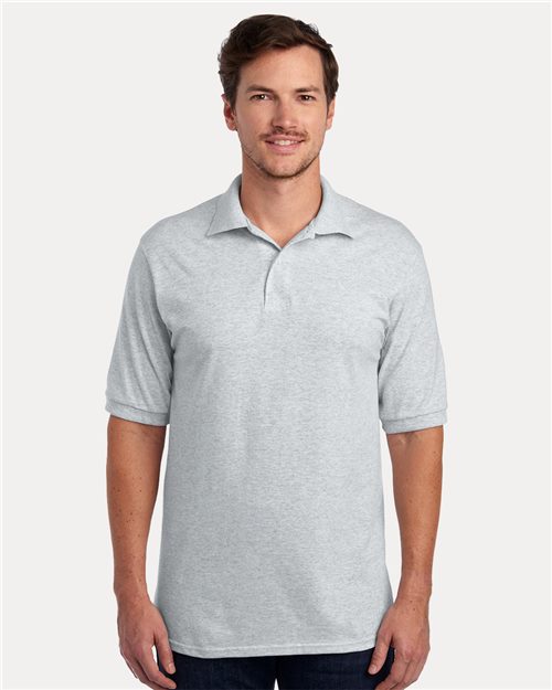 Load image into Gallery viewer, A person smiles with hands by their sides while wearing a light gray JERZEES - Dri-Power® Polo, made from sustainably-sourced cotton, paired with dark jeans against a plain white background.
