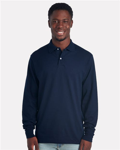 A person models the JERZEES - Dri-Power® Long Sleeve Polo in navy blue, made from sustainably-sourced cotton, against a white backdrop. They stylishly pair it with light-colored jeans for an effortlessly chic appearance.