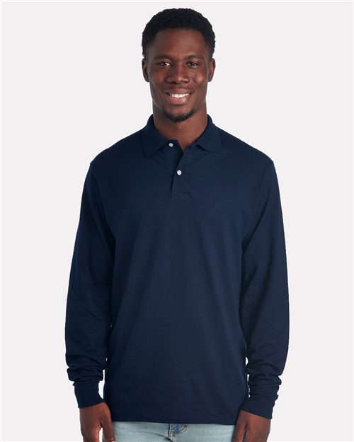 A person models the JERZEES - Dri-Power® Long Sleeve Polo in navy blue, made from sustainably-sourced cotton, against a white backdrop. They stylishly pair it with light-colored jeans for an effortlessly chic appearance.