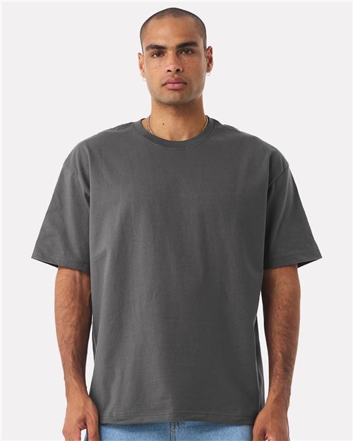 Load image into Gallery viewer, A person wears a BELLA + CANVAS - 7.5 oz Heavyweight Tee, showcasing its simple gray design with a unisex silhouette, paired with light blue jeans. Standing against a white backdrop, the individual has short hair and facial hair, maintaining a neutral expression and relaxed posture with hands at their sides.
