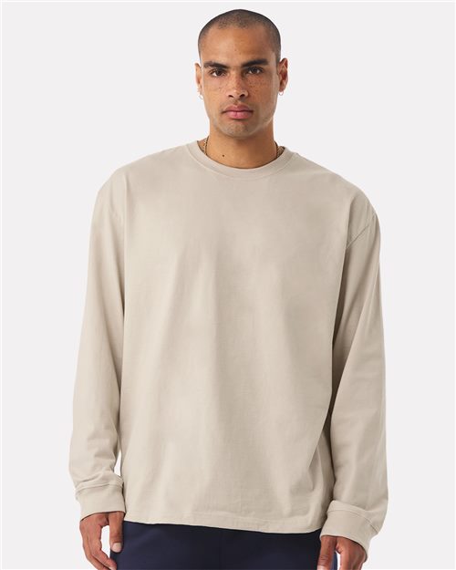 Load image into Gallery viewer, Wearing the BELLA + CANVAS 7.5 oz Heavyweight Long Sleeve Tee in beige and dark pants crafted with Blue Sign certified dyes, a person stands against a plain white background. With a neutral expression, they embody a unisex silhouette that exudes timeless sustainability while looking straight ahead.
